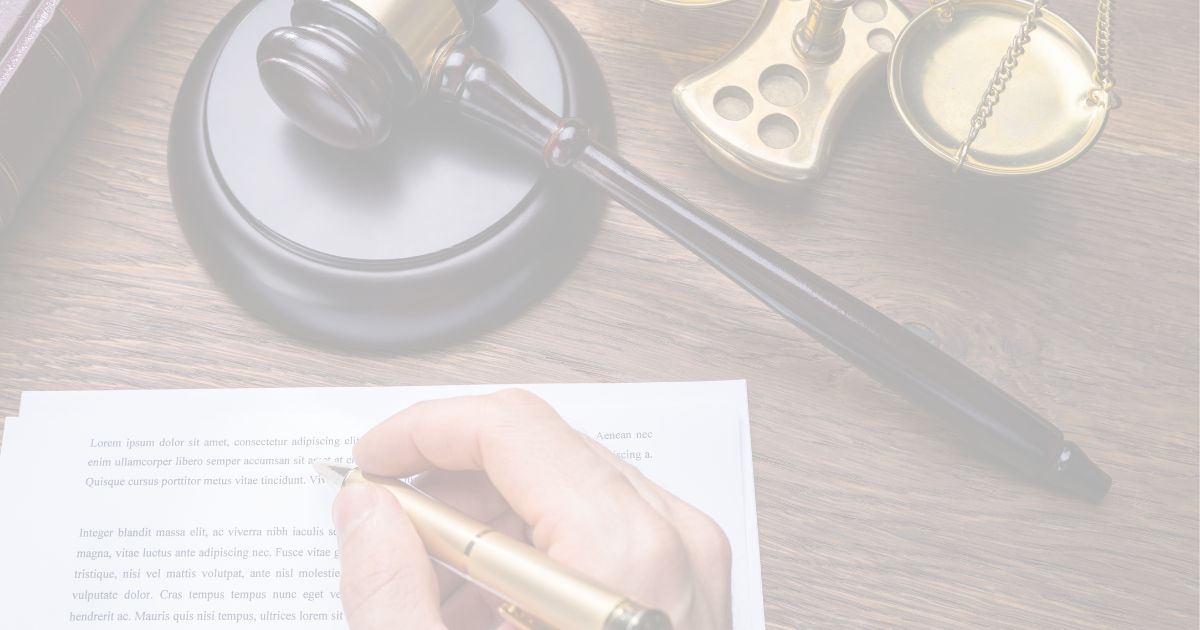 Close-up of a person signing a document with a pen on a wooden desk, with a judge’s gavel and scales of justice in the background.